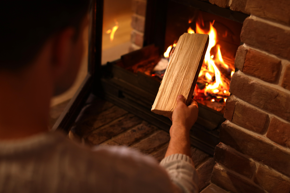 Placing wood into wood-burning fireplace to maintain the flame