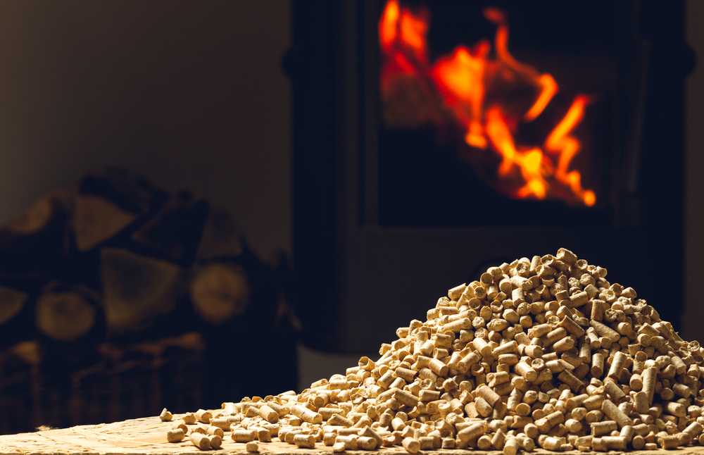 Pellets used for a pellet stove laying in a pile on a table in front of a burning pellet stove